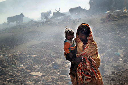野焼きの煙が充満する中、１歳の弟をあやすモハンマド・ルビナさん。スラムで生活するこの家族にはルビナさんを含め弱視が多い＝パキスタン・カラチ郊外で２０１２年３月２１日、小川昌宏撮影