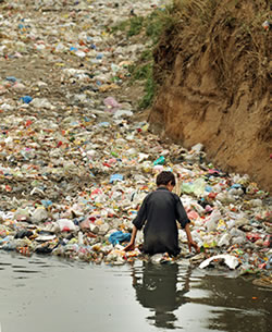 腰まで水につかり、川に浮かんだごみの中から売れそうなものを探す少年＝パキスタン・ラワルピンディで、小川昌宏撮影