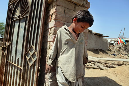 洪水で自宅を流された少年。強い日差しが照りつける青空の下、唯一残った門の周りで遊んでいた＝パキスタン・バディン郡ラルバクシ村で、小川昌宏撮影
