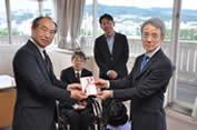 宝塚市ゴルフ場協議会の小堂剛裕会長（左）から寄付金の目録を受け取る毎日新聞大阪社会事業団の森野茂生常務理事（右）。（後方左から）木村佳友さんと森臨太郎市長＝同市役所で２０２５年５月２７日午後５時２５分、関谷徳撮影