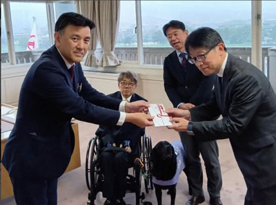 塚市ゴルフ場協議会の坂野文彦会長（左）から寄付金を受け取る毎日新聞大阪社会事業団の濱弘明常務理事（右）、（後方左から）木村佳友さんと森臨太郞市長＝宝塚市役所で