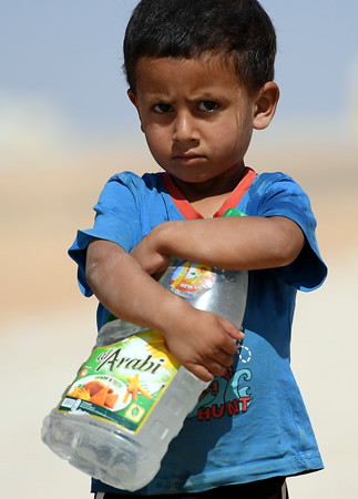水が入ったペットボトルを抱える３歳の男の子。水道がある広場と居住用のコンテナを往復するのが日課だ＝ヨルダン・ザルカ県のアズラック難民キャンプで、久保玲撮影