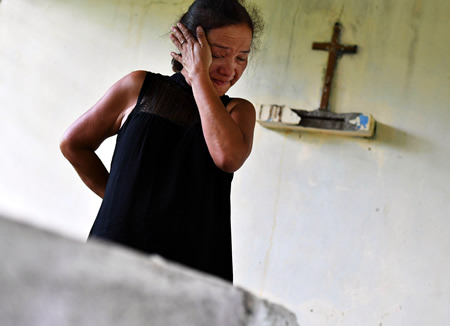 水銀中毒で亡くなった息子の墓の前で、涙をぬぐうチャリト・アベリャーノ・エルカノさん＝フィリピン・カマリネスノルテ州ホセパガニバンで