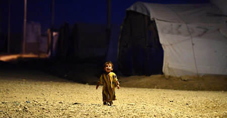 灼熱の避難民キャンプに夜のとばりが下り、テントから外に出た女の子がひとりたたずむ＝イラク・ニナワ県のハゼルＭ１キャンプで