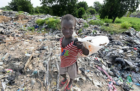 道路脇に積み上げられたゴミ山の中から、金属やプラスチックなどを集める少年。次々とゴミが集まり、異臭を放っていた