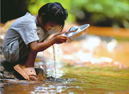タイ国境を流れる川で食器を洗う子ども=ミャンマー・カイン州で2026年6月4日、久保玲撮影